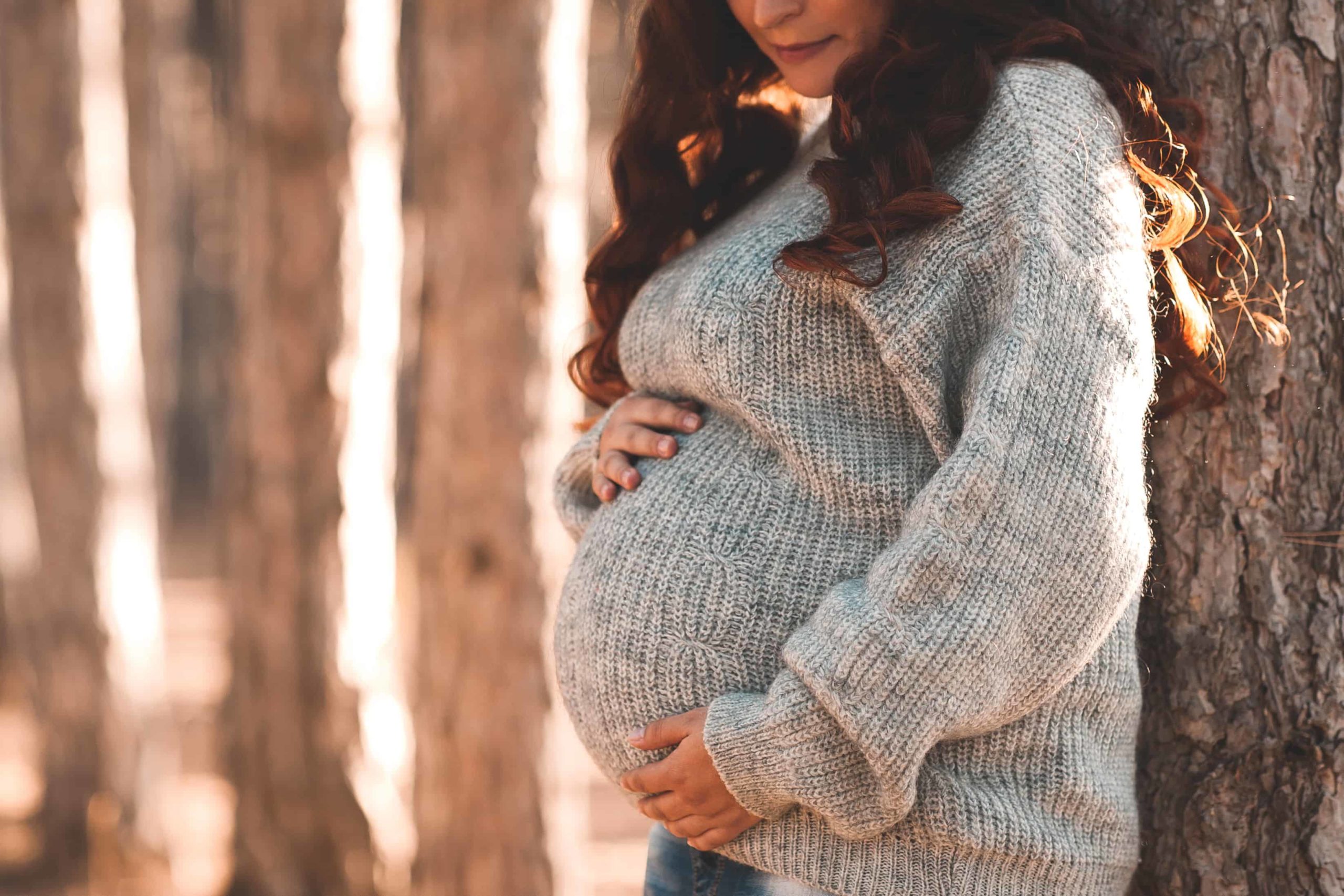 Pregnant woman 30-35 year old wearing warm knitted sweater posing outdoors. Motherhood. Maternity. Autumn season.