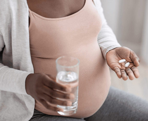 Pregnant woman taking her prenatal with water