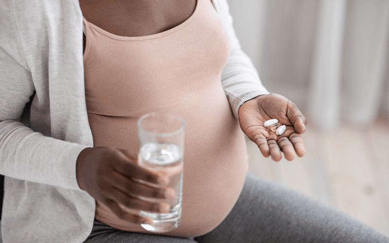 Pregnant woman taking her prenatal with water