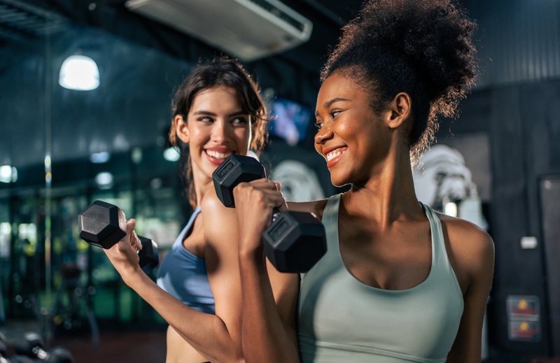 Portrait of African american and Latino sportswoman exercise in gym. Attractive active athlete girls in sportswear workout by lifting weight dumbbells to build muscle for health care and at fitness